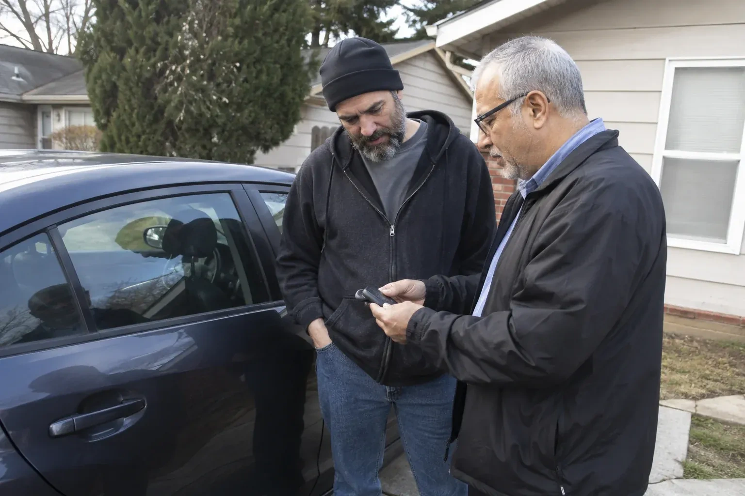 Two adults discussing a key fob beside a parked car. — Car Lockout Service, Welland