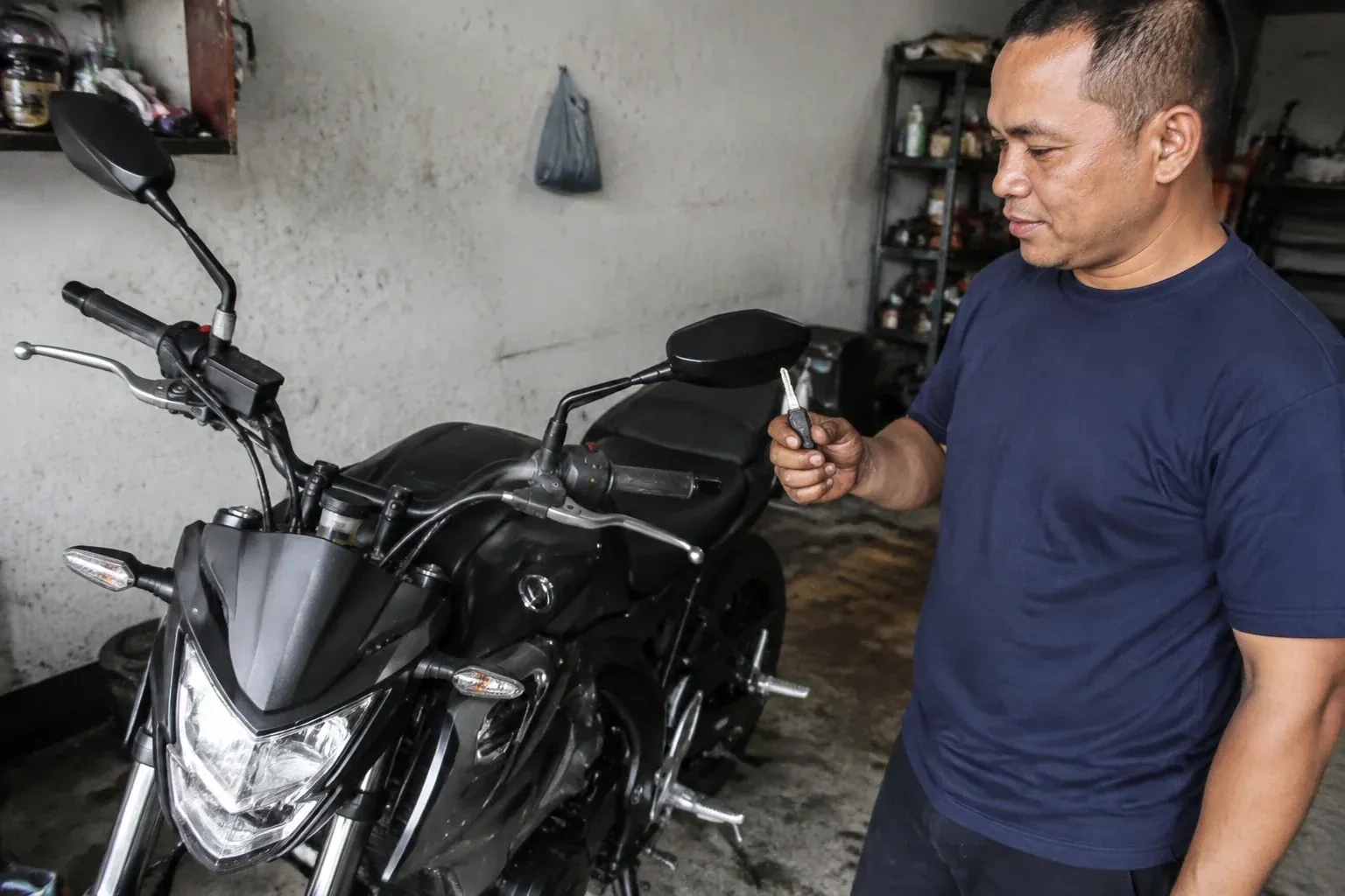 Person holding a key beside a black motorcycle in a garage. — Motorcycle & Scooter Keys, Welland