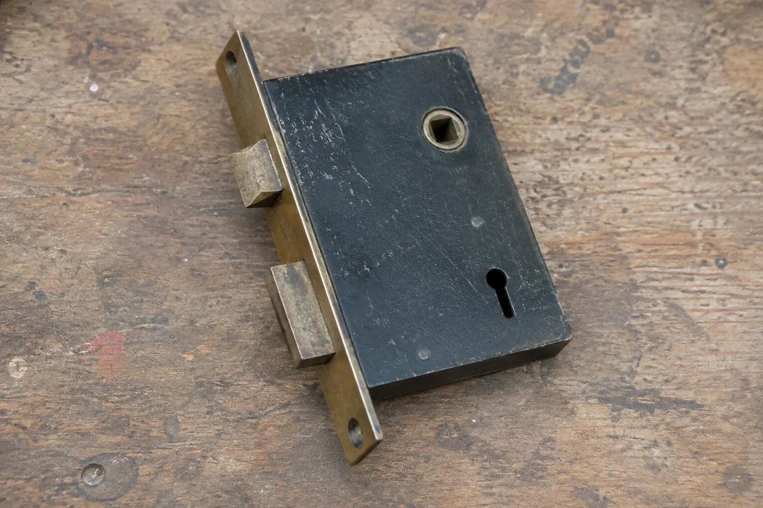 Closed mortise lock case with spindle opening, keyhole, latch and deadbolt on a wooden workbench. — Vintage Mortise Lock Service, Fenwick