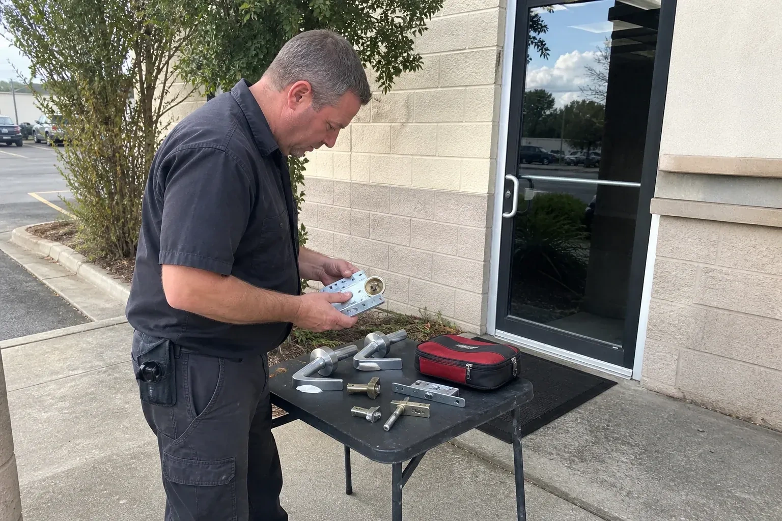 Technician examining detached commercial lock hardware on a table outside a shop entrance. — Business Lockout Service, Welland